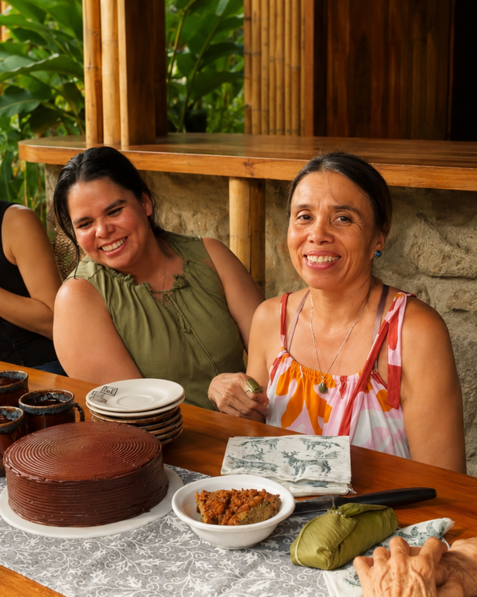 Dos mujeres conversando en el jardín de Niuvaluna, con el río y la selva de fondo